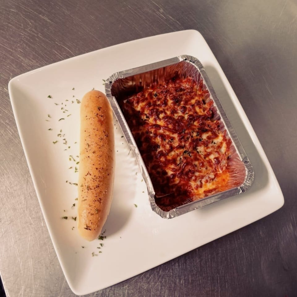 Midway Bar and Grill's baked pasta in a foil container with a breadstick on a white plate.
