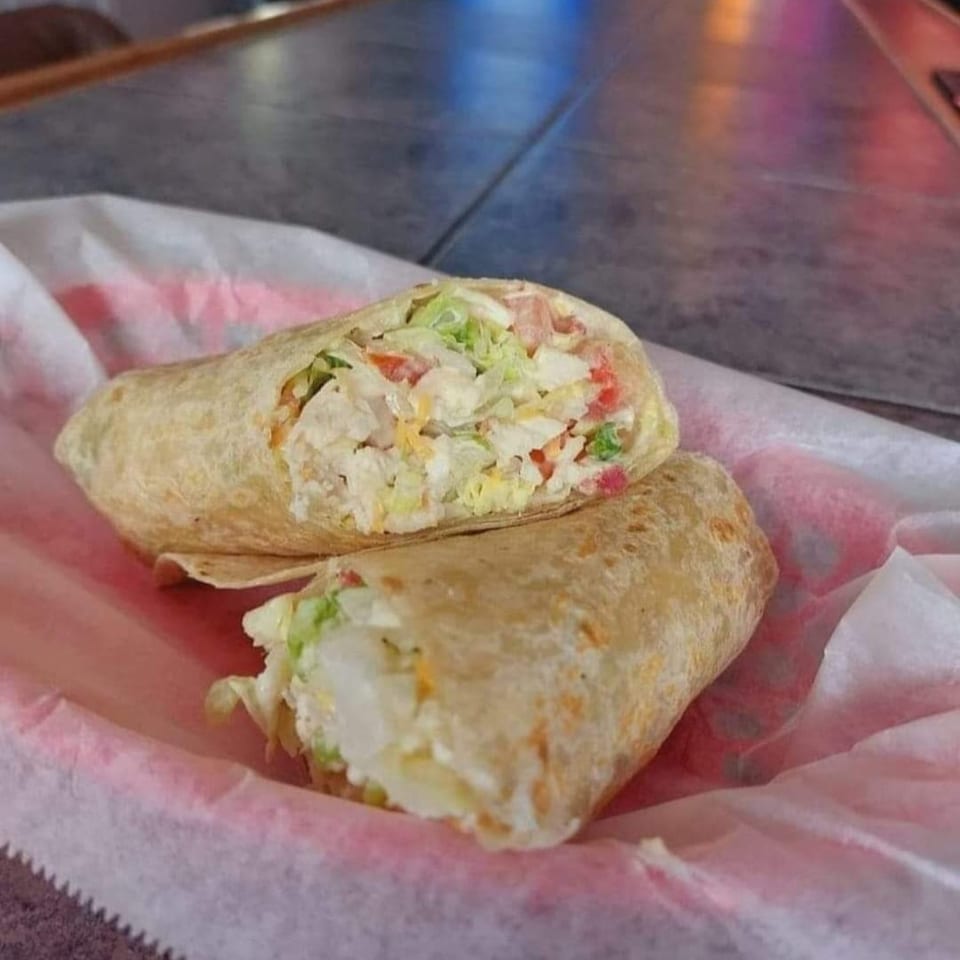 Two halves of a chicken wrap, filled with lettuce, tomato, and cheese, in a red paper-lined basket.